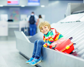 Kleiner Junge sitzt am Flughafen auf dem Gepäckband.