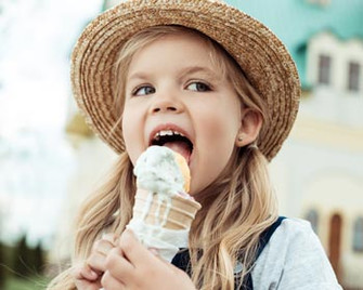 Kind, ein Mädchen, isst ein Eis und trägt einen Strohhut im Familienurlaub.