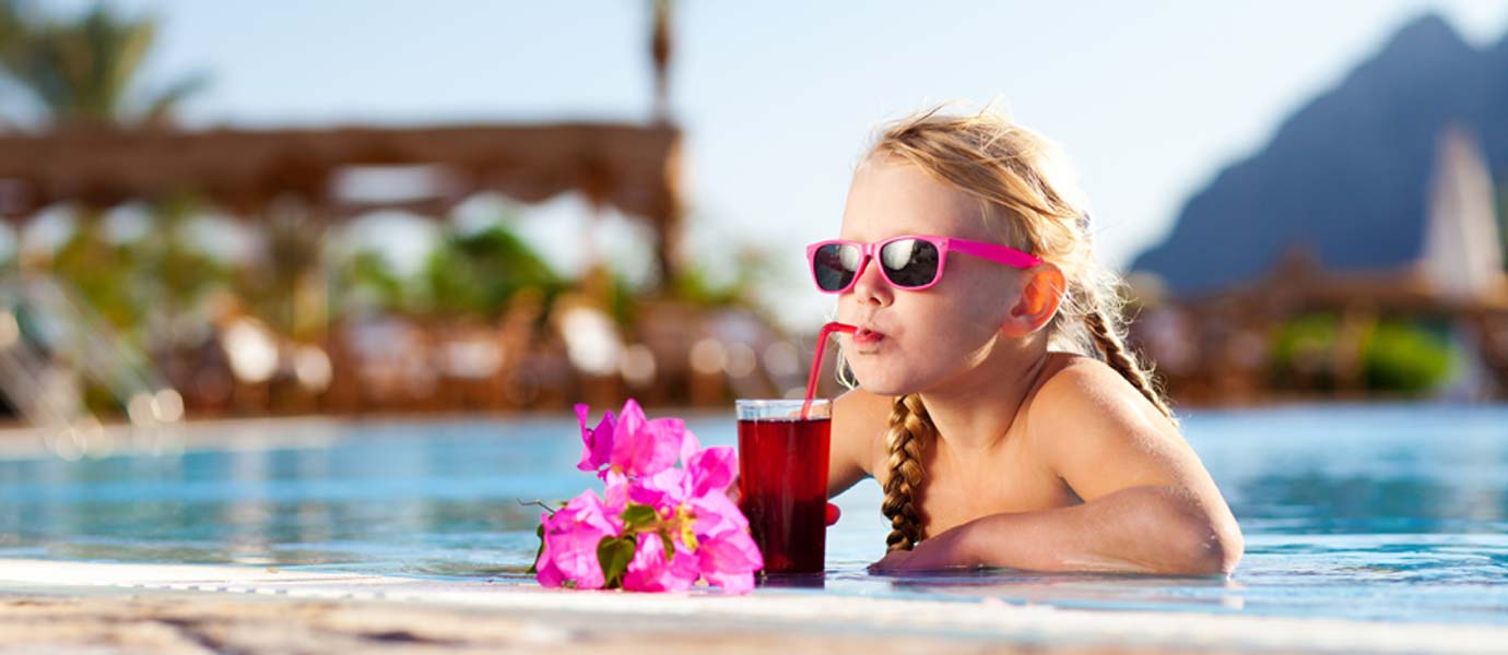 Kleines Mädchen mit Sonnenbrille trinkt Cocktail am Pool