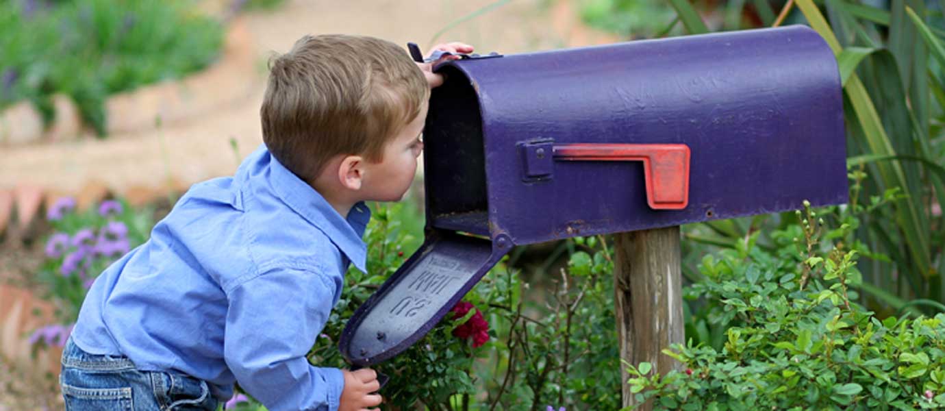Kleiner Junge steht vor einem Briefkasten und schaut hinein.
